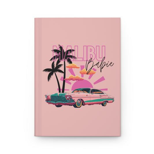 Notebook with pastel pink 'Malibu Babie' design featuring a pink vintage car, palm trees, and orange clouds and pink sun on a pink background